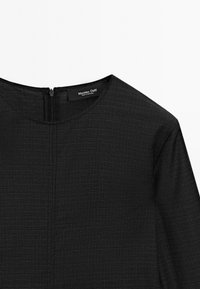 Svart klänning med en texturerad yta, med rund halsringning och en dold dragkedja bak. Taggen som syns läser "Massimo Dutti."