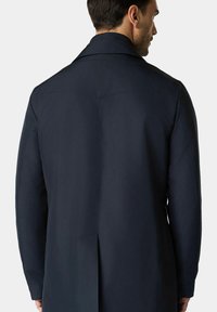 Cappotto lungo blu navy con una texture liscia, colletto classico e spacco centrale sul retro. Presenta un taglio sartoriale e cuciture pulite.