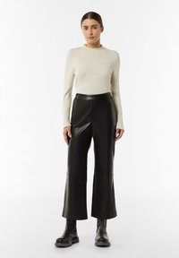Zwarte leren broek met wijde pijpen, voornaden, hoge taille en een soepele textuur. Gepaard met een lichtcrème, strak fitting langemouwen top.