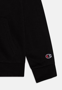 Sudadera negra con una textura suave, que cuenta con un bolsillo frontal, puños acanalados y un pequeño logo bordado en la manga.
