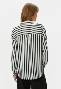 Blusa de rayas en blanco y negro con cuello y puños abotonados, y una textura ligera. La parte posterior tiene un detalle de yugo.