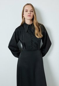 Black dress with long sleeves, buttoned front, and a pointed collar. Made of a smooth fabric with a flowing silhouette.