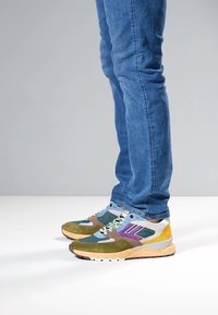 Multicolored sneakers featuring green, brown, yellow, and blue sections, with a textured upper and a light-colored sole.