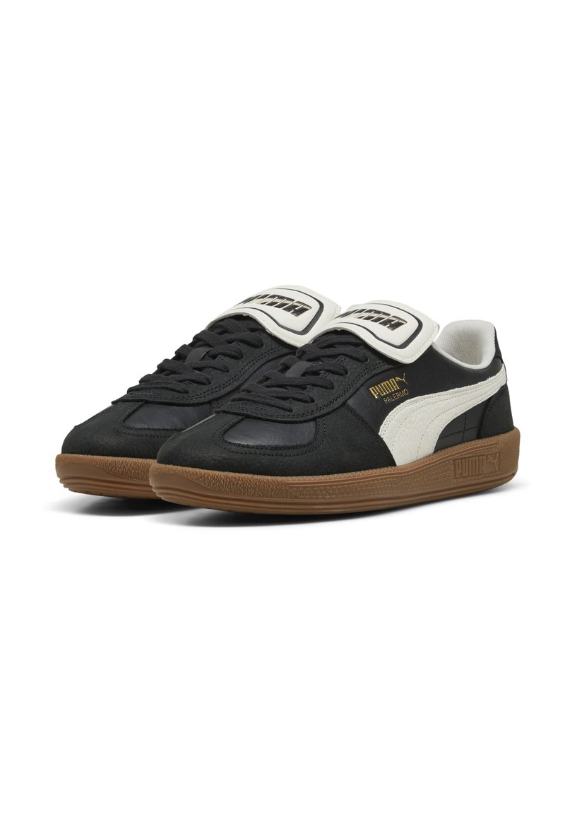 Baskets noires avec des accents blancs, présentant un dessus texturé, un bout rond et une épaisse semelle en caoutchouc marron. Logo "PUMA" sur la languette et sur le côté.