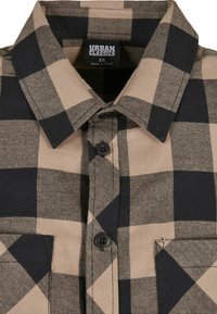 Chemise en flanelle à carreaux bruns et noirs avec un devant boutonné, deux poches poitrine et un col ; comprend une étiquette tissée à l'intérieur.