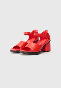 Red leather open-toe sandals featuring a wide front strap, adjustable ankle strap, and a chunky black heel. Smooth texture with minimalist design.