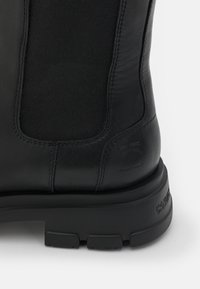 Bottine en cuir noir avec panneau latéral élastique, logo embossé sur le talon et semelle crantée épaisse.