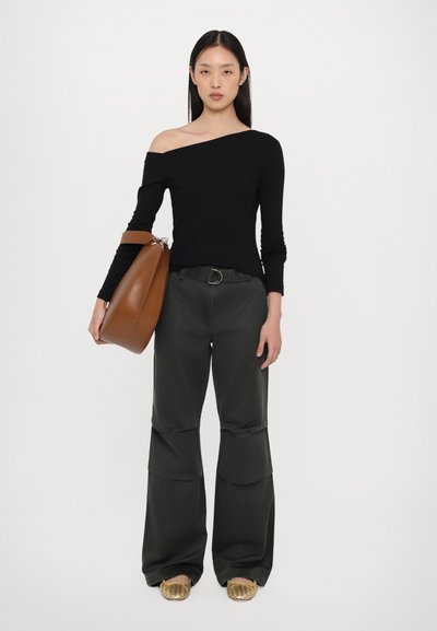 Zwart geribd off-shoulder top, donkergroene wijde broek met naden, bruine leren handtas en gouden loafers met een gestructureerde afwerking.