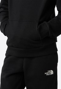 Fekete kapucnis pulóver és melegítőnadrág puha anyagból. Bordázott mandzsetták és derékpánt. Fehér logó található a combon.