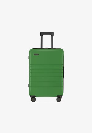 Groene harde koffer met een gladde, glanzende afwerking. Voorzien van een telescopische handgreep, vier draaipunten en horizontale ribbels op het oppervlak.