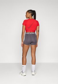 Czerwony krótki podkoszulek sportowy z logo Nike, zestawiony z szarymi szortami z wysokim stanem i paskiem "PRO". Białe skarpetki i buty.