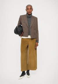 Bruin houndstooth blazer, grijze coltrui, crèmekleurig shirt, brede katoenlook broek in mosterdgeel, zwarte tas, grijze sokken en twee-kleurige schoenen.