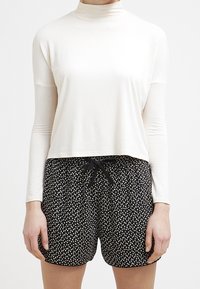 Haut blanc à manches longues et col roulé associé à un short noir avec un motif de pois blancs et un cordon noir à la taille.