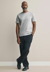 Grijze katoenen t-shirt met korte mouwen, gecombineerd met zwarte broeken en zwarte schoenen. Eenvoudig ontwerp tegen een neutrale achtergrond.