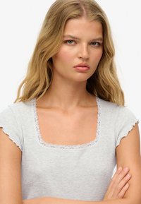 Grå rippet t-shirt med korte rynkede ærmer og en firkantet halsudskæring, der har en delikat blondekant. Enkel design, blød tekstur.