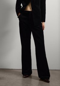 Schwarzes Samtanzug mit einem maßgeschneiderten Blazer und weit geschnittenen Hosen. Auffällige glatte Textur und elegantes Design mit einem diskreten Taschendetail.
