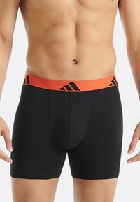 Svarta boxerkalsonger med ett orange elastiskt midjeband, med svarta logotypdetaljer och en figurnära design. Slät tygtextur.