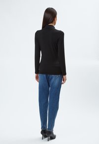 Schwarzes Langarmoberteil mit hohem Kragen, kombiniert mit hellblauen Jeans und schwarzen High Heels, von hinten betrachtet. Glatte Textur.