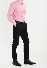 Camicia a righe rosse e bianche, pantaloni neri e stivali alla caviglia neri. La camicia ha un collo standard e maniche lunghe.