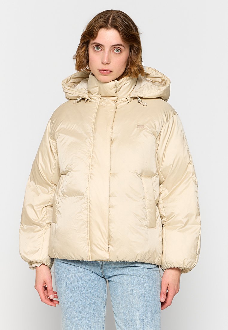 Chaqueta de plumas beige con cuello alto y capucha, que presenta una textura brillante, puños elásticos y dos bolsillos frontales.