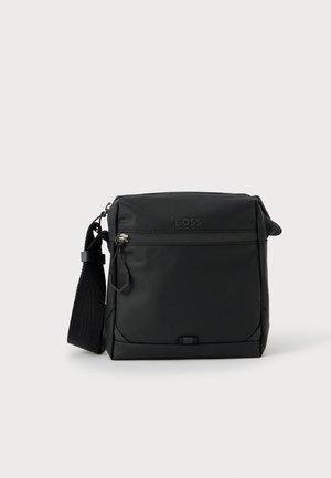 Mala tiracolo preta em material liso e mate com bolso frontal com fecho de correr, detalhe de logótipo e alça ajustável. Forma retangular compacta.