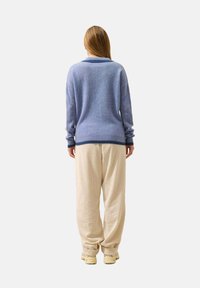 Svetle modrý svetr s ribbed lemem a límcem, doplněný béžovými širokými kalhotami s texturou. Model stojí zády, aby ukázal zadní stranu outfitu.
