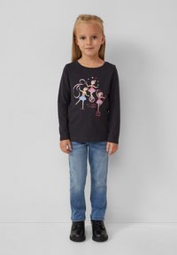 Dugih rukava tamnosiva majica s raskošnim grafičkim prikazom plesača, uparena s svijetloplavim trapericama i crnim čizmama. Jednostavan, ležeran outfit.