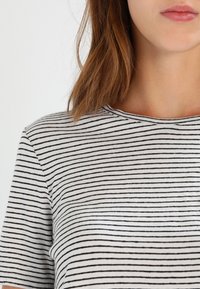 Camiseta de rayas con cuello redondo, hecha de una tela suave, presenta finas rayas negras sobre un fondo blanco. Mangas cortas casuales.