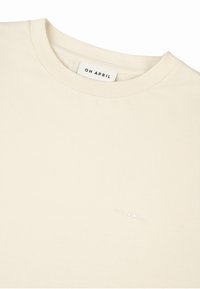 Krémové tričko z měkké bavlny s klasickým kulatým výstřihem. Na přední straně je jemně vyražené logo "OH APRIL".