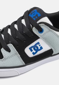 Harmaa ja musta lenkkari, jossa on teksturoitu päällinen, siniset korostukset, mustat nauhat ja valkoinen pohja, ja sivussa on suuri DC-logo.