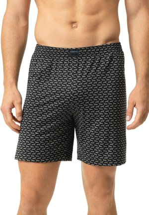 Männlicher Torso trägt schwarze Boxershorts mit kleinem weißem Pferdemuster, steht mit entspannten Händen an den Seiten.