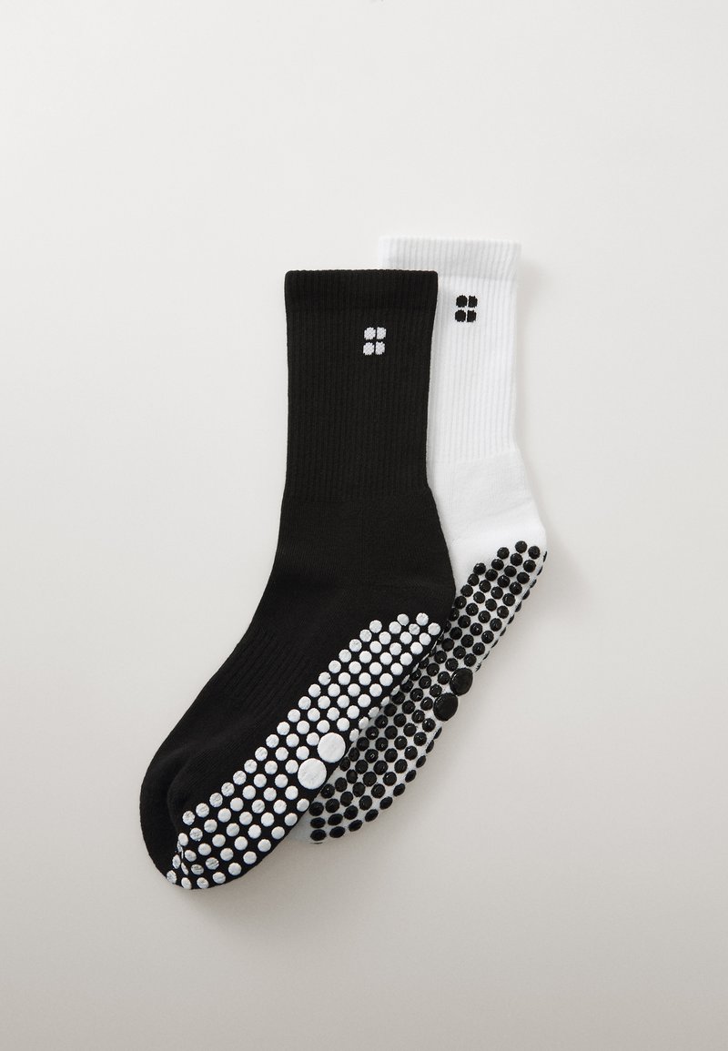 Two pairs of knee-length socks: one black with white rubber grip dots and two white dots, the other white with black grip dots and two black dots.