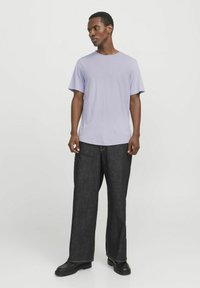 Tricou din bumbac de culoare violet deschis, cu mâneci scurte, asociat cu pantaloni largi din denim închis. Încălțămintea neagră completează ținuta.