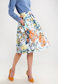 Blommig knälång kjol med ljusblå bas, prydd med mönster i orange, gult och marinblått; inkluderar fickor och en strukturerad plisserad design.