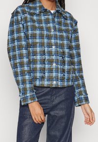 Kariertes Jackett in Blau und Olivgrün, mit einem verkürzten Design, strukturiertem Stoff, Knopfverschluss und fransigen Säumen.