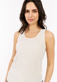 Canotta beige chiaro con texture a coste, scollatura rotonda e spalline larghe. È caratterizzata da un tessuto morbido e una vestibilità rilassata.