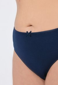 Marineblauwe katoenen bikinislip met een gladde textuur, voorzien van een klein strikaccent op de tailleband en een middelhoge snit.