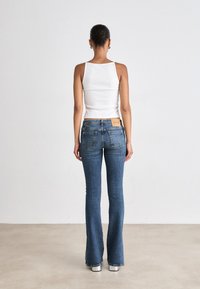 Kohandatud valge särk, millel on sinised laienevad teksad, millel on paelaga mündilabel ja kontrastsed õmblused. Sujuv denimitekstuur.