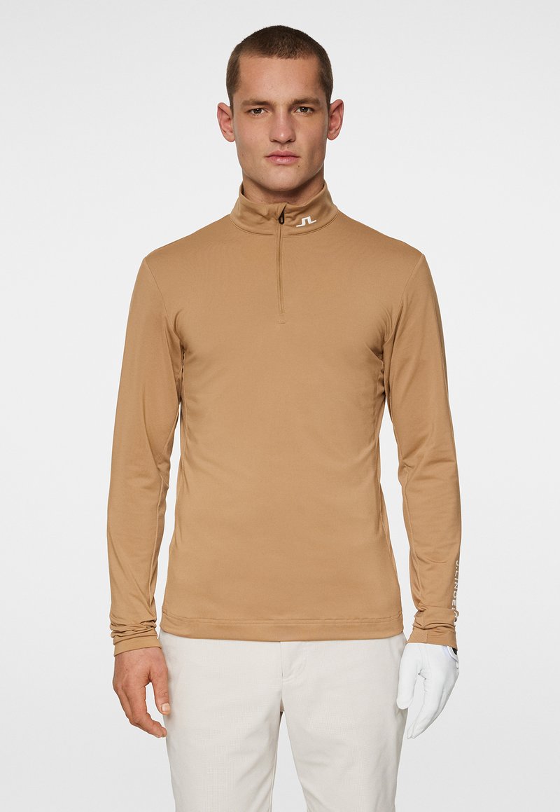 Jasnobrązowa, długorękawowa polo z wysokim kołnierzykiem i półzamkiem. Wykonana z gładkiego, elastycznego materiału. Posiada logo na kołnierzyku i rękawie.