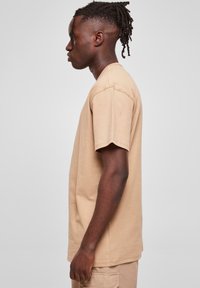 Tricou din bumbac bej, cu mâneci scurte, de tip crew neckline și o croială lejeră. Textură netedă, cu accente de cusătură vizibile.