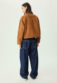 Brun denimjakke med en corduroy krave, parret med løstsiddende, mørkeblå vide jeans og hvide sneakers. Enkelt design, ingen mønstre.