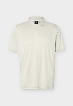 Μπεζ κοντομάνικη πόλο μπλούζα με γιακά και δύο κουμπιά, παρουσιασμένη μπροστά σε απλό ανοιχτό φόντο.