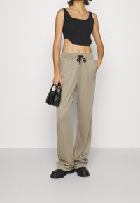Czarny krótki top, beżowe spodnie z gumką i czarna torebka teksturowana. Spodnie mają luźny krój i boczne kieszenie. Czarne buty na platformie.
