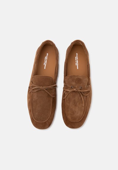Paire de mocassins en daim marron avec détail nœud à l'avant et bouts arrondis, vus d'en haut sur fond blanc.