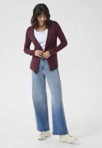 Bordeaux langermet cardigan med åpen front, lagt over en hvit topp og kombinert med lyseblå vide jeans og hvite sneakers.