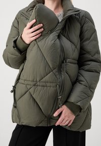 Oliwkowo zielona pikowana kurtka puchowa z wysokim kołnierzem, wyposażona w boczne zamki błyskawiczne i detale ze ściągaczem dla regulacji. Gładki, ocieplany materiał.