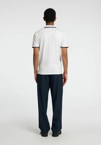 Polo shirt blanc avec des accents noirs, manches courtes et un col classique, associé à un pantalon marine foncé et des chaussures noires.