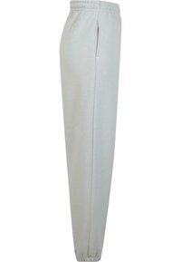 Lys grå joggebukser med en elastisk midje, sidelommer og elastiske mansjetter ved anklene, laget av myk bomullsmateriale.