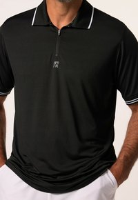 Polo noir avec col zippé, manches courtes et accents de rayures blanches sur les manches. Présente un petit logo sur la poitrine. Texture de tissu douce.