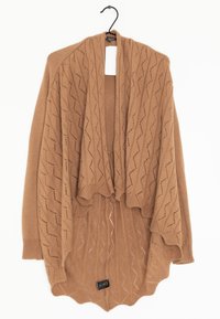 Brun stickad sjal med ett texturerat zigzag-mönster, öppen framsida och skulpterad fåll, hängande på en svart krok mot en vit bakgrund.